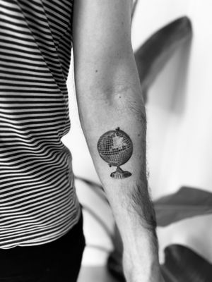 A black and gray micro-realism tattoo by Timmy featuring a detailed earth globe and shimmering disco ball.