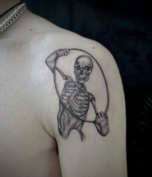 Micro-realistic black and gray tattoo featuring a hoop symbolizing life and death, with a skeleton and person in a delicate balance by Kateryna Goshchanska.