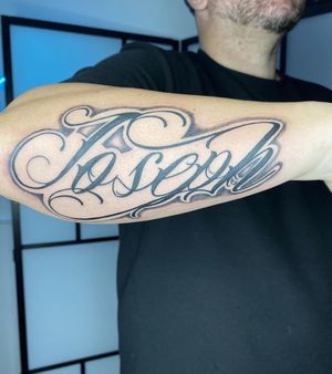 Get a stunning black and gray chicano lettering tattoo done by the talented artist Alfonso Barberio. Perfect for those looking for a bold and stylish design.