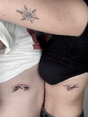 Elegant black and gray fine line tattoos of matching hands symbolizing creation, by talented artist Alina Amberland.