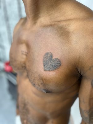 This illustrative tattoo by Alex Caldeira combines a heart motif with a unique fingerprint design on dark skin. A striking and meaningful piece of body art.