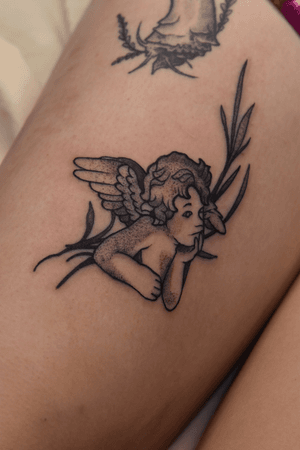 A black and gray illustrative tattoo of an angelic cherub, intricately detailed by artist Iva M.