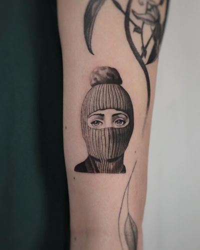 Black and gray micro-realism tattoo of a woman wearing a Fornasetti balaclava mask by Constanza.