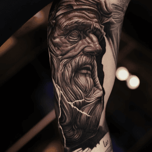 Ember's black and gray realism tattoo features a striking image of Zeus with lightning, capturing the power and majesty of the mythological deity.