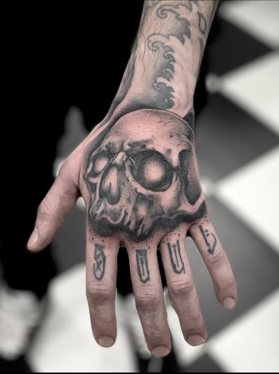 A black and gray tattoo of a detailed skull, created by artist Cara Hayward, in a realistic style.