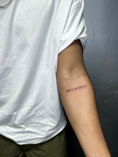 Small lettering tattoo of Roman numerals done by artist Inna, featuring delicate fine line work.