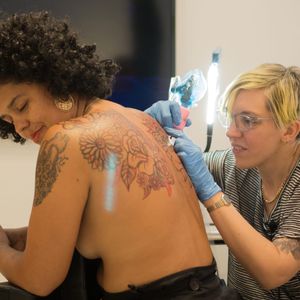 Emily North tattoos fellow artist Awilda Rodríguez Lora on a livestream at SOHO20 Gallery for their collaboration "Still Life, Still Alive" (Photo by Amar Puri.) #Art #Feminism #LiveTattoo #NYC #EmilyNorth #Em16 #AwildaRodríguezLora