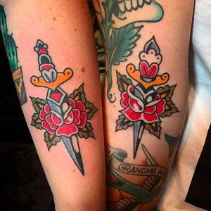 Matching tattoos of two daggers and two roses. Amazing work by Jacob N. #JacobN #traditionaltattoo #boldtattoo #oldschool #rose #dagger #matchingtattoos #traditional