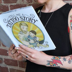 A tattooed woman holding Tell Me a Tattoo Story by Alison McGhee. #AlisonMcGhee #childrensbooks #ElizaWheeler #TellMeaTattooStory