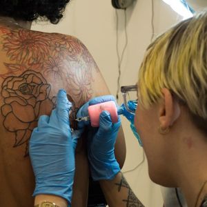 Emily North tattoos fellow artist Awilda Rodríguez Lora on a livestream at SOHO20 Gallery for their collaboration "Still Life, Still Alive" (Photo by Amar Puri.) #Art #Feminism #LiveTattoo #NYC #EmilyNorth #Em16 #AwildaRodríguezLora