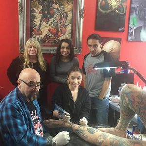 A photograph of the Rand family and others observing Kiara doing some tattooing. #apprentice #DaveRand #ChrisRand #familybusiness #KiaraRand