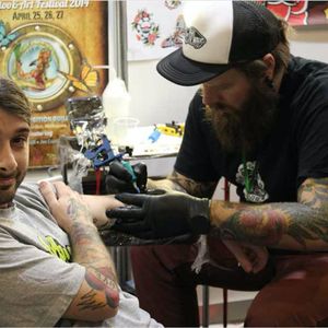 A photograph of Moses D Mezoghlian tattooing one of his clients (IG—moses_d_mezoghlian).