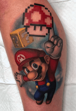 Super mario tattoo, mixed style in color. It shows an illustrative Mario reaching for a pixelated/ geometric mushroom