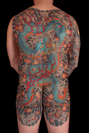 Experience the power and beauty of a Japanese dragon entwined with delicate sakura flowers in this stunning back piece tattoo by renowned artist Stewart Robson.