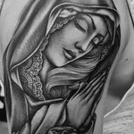 Get inked with a stunning Chicano style Mother Mary tattoo on your upper arm in London, GB. Symbolize faith and love with this beautiful design.
