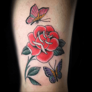 Get inked by Eddy Ospina with this vibrant traditional tattoo featuring a butterfly and flower motif, perfect for your upper arm.