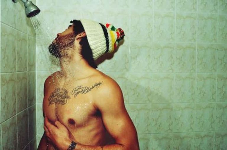 Two script tattoos across the chest, under a running shower.