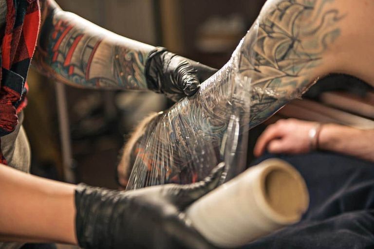 An artist wraps a fresh arm tattoo in plastic film.